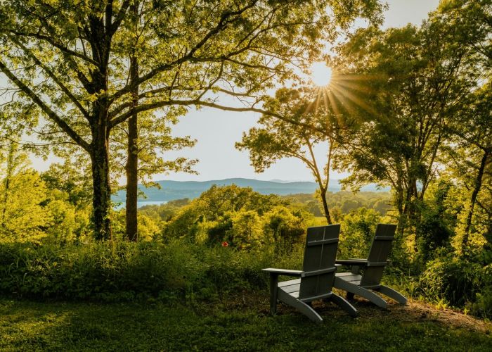 Two outdoor chairs beneath leafy trees overlooking the Hudson Valley countryside, with sunlight filtering through the trees.
