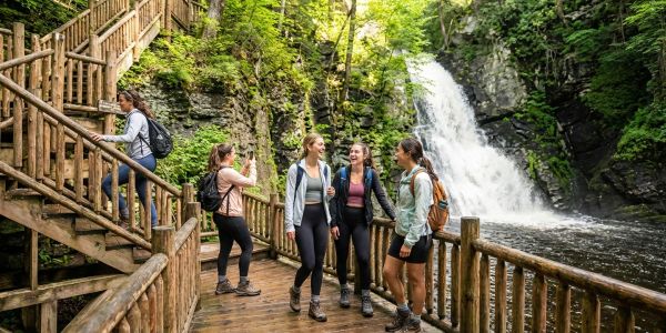 Friends hiking on a wooden trail near a scenic waterfall in the Pocono Mountains.