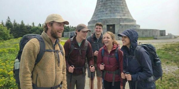 Group of hikers with backpacks standing near a historic stone monument on a scenic trail in the Berkshires.